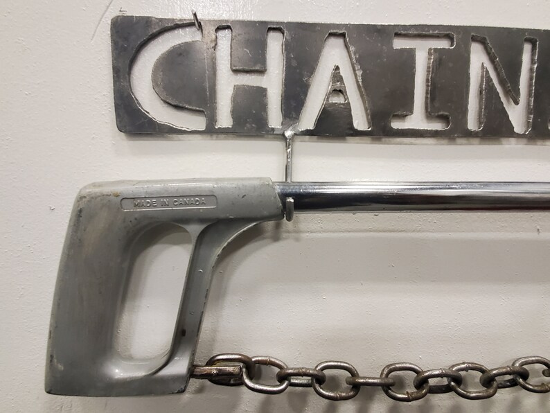May include: A silver metal saw with a gray plastic handle and a chain attached to the end. The saw is labeled "Made in Canada".