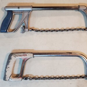May include: Two vintage hand saws with chains. The top saw has a blue handle and the bottom saw has a white handle with the text "Eclipse 307" printed on it.