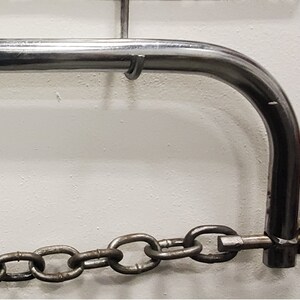 May include: A silver metal chain attached to a silver metal hook. The hook is attached to a silver metal bar.