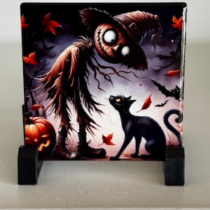 May include: A Halloween-themed decorative tile featuring a scarecrow and a black cat. The scarecrow has a stitched smile and large eyes. The cat is looking up at the scarecrow. Red leaves and bats are scattered around the scene. The tile is displayed on a black stand.