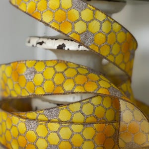 Op de afbeelding: Geel en grijs decoratief lint met een honingraatpatroon. Het lint is gewikkeld rond een witte, verweerde sokkel. Het honingraatontwerp heeft tinten geel en oranje, met een grijze achtergrond.