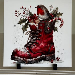 Op de afbeelding: Een aquarel illustratie van een rode werklaars gevuld met kerstversieringen. Een kleine vogel zit bovenop de laars, die gevuld is met een cadeau, hulst en een zuurstok. Sneeuw accentueert de scène.