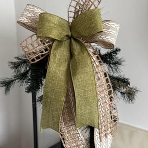 May include: A green and brown bow with a burlap and white patterned ribbon. The bow is tied on a black lantern.