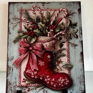 May include: A festive wooden plaque depicting a red Christmas boot overflowing with holly, berries, and candy canes. The boot is adorned with a large red and white striped bow and white floral patterns. The background is a distressed blue with a red and white striped border.