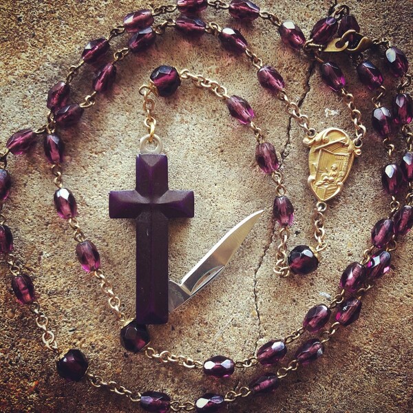 Purple cross bone knife pendant on a vintage amethyst glass rosary.