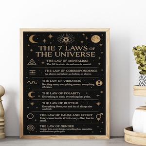 May include: A framed print with the text "The 7 Laws of the Universe" in gold lettering on a black background. The print includes symbols and text describing each law. The frame is a light brown color.