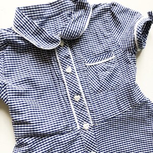 Puede incluir: Vestido a cuadros azul y blanco con cuello y ribete blancos. El vestido presenta botones en forma de coraz&oacute;n y un peque&ntilde;o bolsillo. Las mangas cortas est&aacute;n rematadas con un ribete blanco y peque&ntilde;os lazos. El vestido es de tejido ligero.