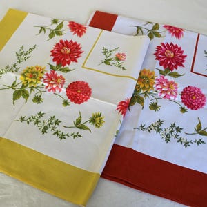 May include: Two rectangular fabric cloths featuring a white centre with a floral pattern of red, pink, and yellow dahlias and green foliage. One cloth has a solid mustard yellow border, while the other has a solid burnt orange border.