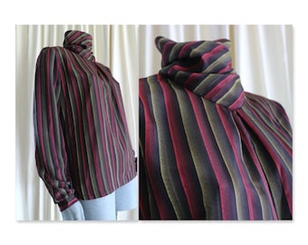 Puede incluir: Una blusa de manga larga a rayas con un cuello alto y fruncido. La blusa está hecha de una tela suave y sedosa y presenta una combinación de colores negro, burdeos y verde oliva.