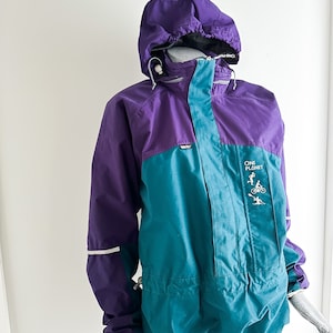 May include: A purple and teal hooded jacket with a zip fastening and a "One Planet" logo on the front. The jacket has a drawstring hood and reflective accents on the sleeves.