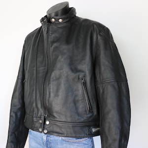 May include: A black leather jacket with a zip-up front, a small pocket on the chest, and a round collar. The jacket has a classic design and is displayed on a mannequin.