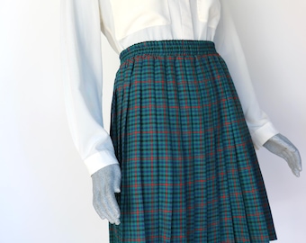 May include: A green, red, and black plaid pleated skirt with an elastic waistband. The skirt is paired with a white long-sleeve button-up shirt with two front pockets. The skirt is knee-length.
