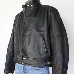 May include: Black leather jacket with a stand-up collar, zipper closure, and multiple pockets. The jacket has a classic design with silver snap details and a fitted silhouette. The jacket is displayed on a mannequin.