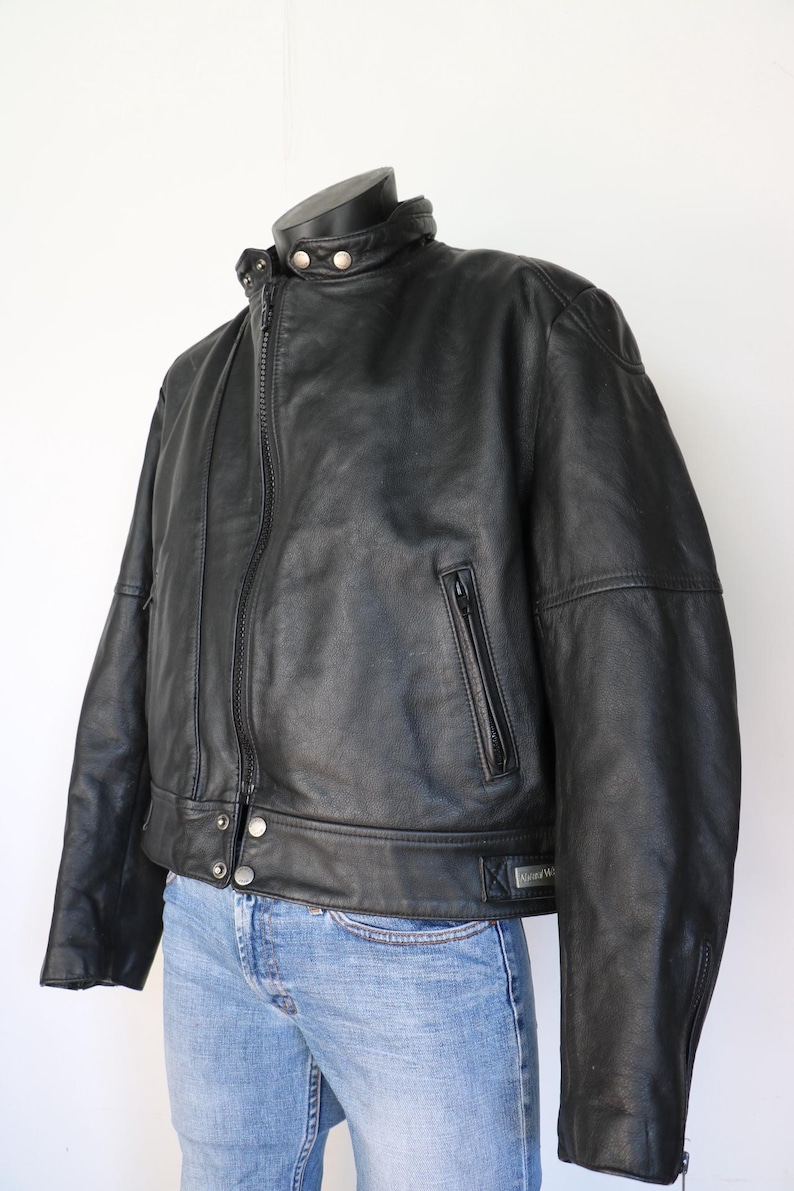 May include: Black leather jacket with a stand-up collar, zipper closure, and multiple pockets. The jacket has a classic design with silver snap details and a fitted silhouette. The jacket is displayed on a mannequin.