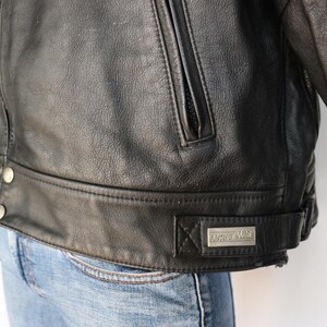 May include: A black leather jacket with a zipper pocket and silver buttons. The jacket has a belt detail at the waist and a small rectangular metal tag that reads "Roper Rider".