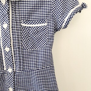 Puede incluir: Vestido de cuadros azules y blancos con cuello, ribete de bolsillo y pu&ntilde;os blancos. El vestido tiene una parte delantera abotonada con botones en forma de coraz&oacute;n. Las mangas cortas est&aacute;n rematadas con ribete blanco.