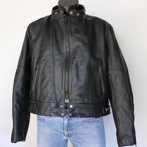 May include: Black leather jacket with a stand-up collar, zipper closure, and multiple pockets. The jacket is displayed on a mannequin and paired with blue jeans. A classic outerwear piece.