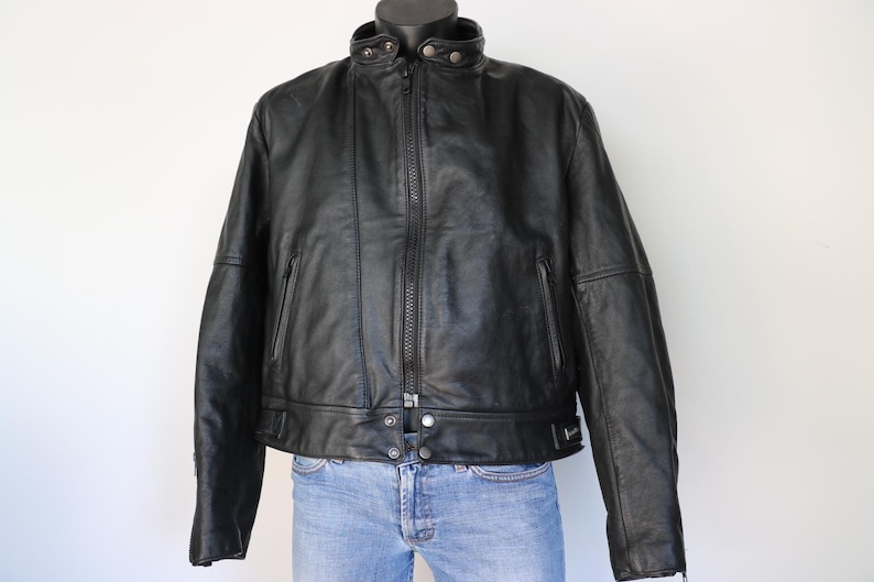May include: Black leather jacket with a stand-up collar, zipper closure, and multiple pockets. The jacket is displayed on a mannequin and paired with blue jeans. A classic outerwear piece.