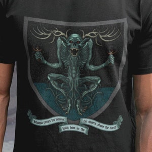 May include: A black t-shirt with a graphic print of a green creature with antlers and a quote: "Always correct, but seldom, both been in the other, for spoilers above the earth".