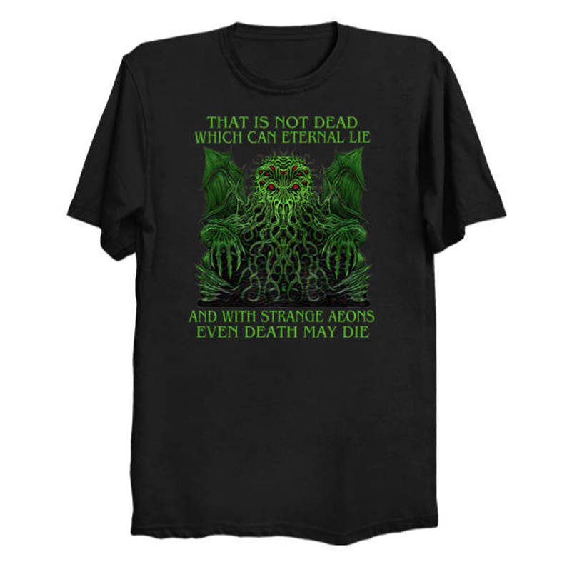 May include: Black t-shirt featuring a green and black graphic of a creature with text that reads "THAT IS NOT DEAD WHICH CAN ETERNAL LIE AND WITH STRANGE AEONS EVEN DEATH MAY DIE".