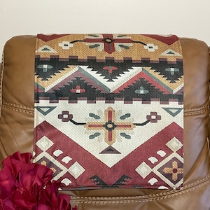 May include: A brown leather recliner with a red, white and black patterned throw pillow on the armrest. The pillow has a geometric design with a southwestern theme.