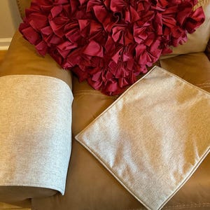 May include: A brown leather sofa with two beige armrest covers and a red ruffled cushion. The sofa has a beige cushion on top of it.