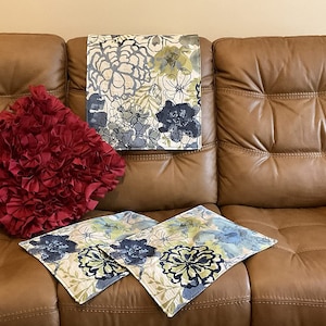May include: A brown leather sofa with three floral patterned throw pillows. Two of the pillows are blue and green, and one is red.