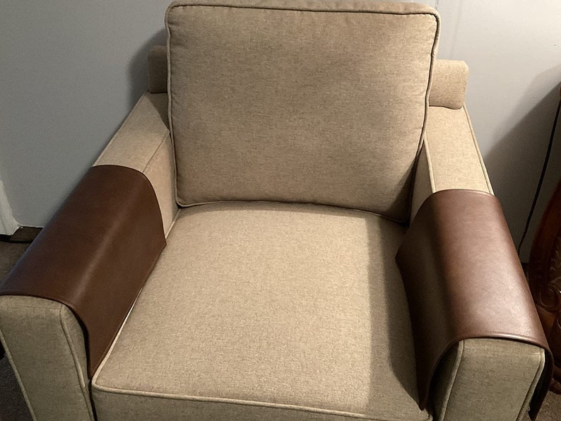 May include: A beige armchair with brown leather armrest covers. The chair has a tufted back and a thick, padded seat.