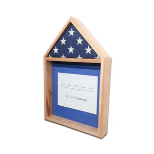 May include: A wooden shadow box with a blue background and a glass insert for a photo. The top of the box is a small triangular roof with a folded American flag.