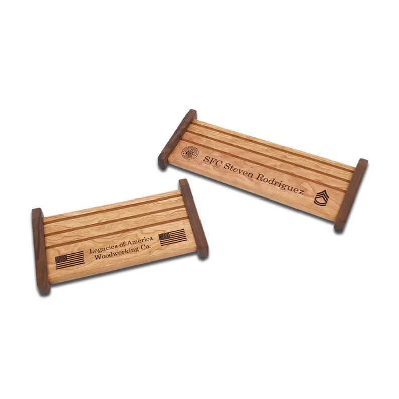 May include: Two wooden display stands for military medals. The top stand is engraved with "SFC Steven Rodriguez" and a military rank insignia. The bottom stand is engraved with "Legacies of America Woodworking Co." and an American flag.