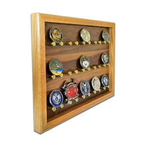 May include: A wooden shadow box with a walnut finish and a light oak frame. The shadow box has 18 slots for displaying challenge coins, each slot is lined with a brass bullet casing. The shadow box is filled with a variety of challenge coins, including military and law enforcement coins.