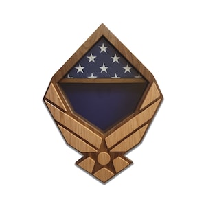 May include: Wooden shadow box with a folded American flag inside. The shadow box is shaped like the Air Force emblem, with wings and a star in the center.