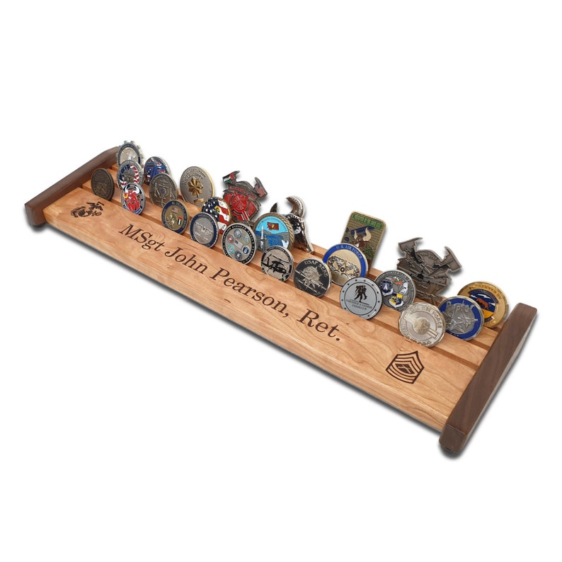 May include: A wooden display rack with a walnut finish holds a collection of military challenge coins. The rack is engraved with the text "MSgt John Pearson, Ret."