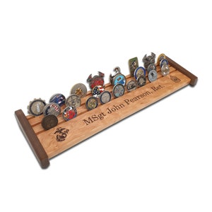 May include: A wooden coin display rack with a cherry finish and walnut accents. The rack has slots for 18 coins and is engraved with the text "MSgt John Pearson, Ret."