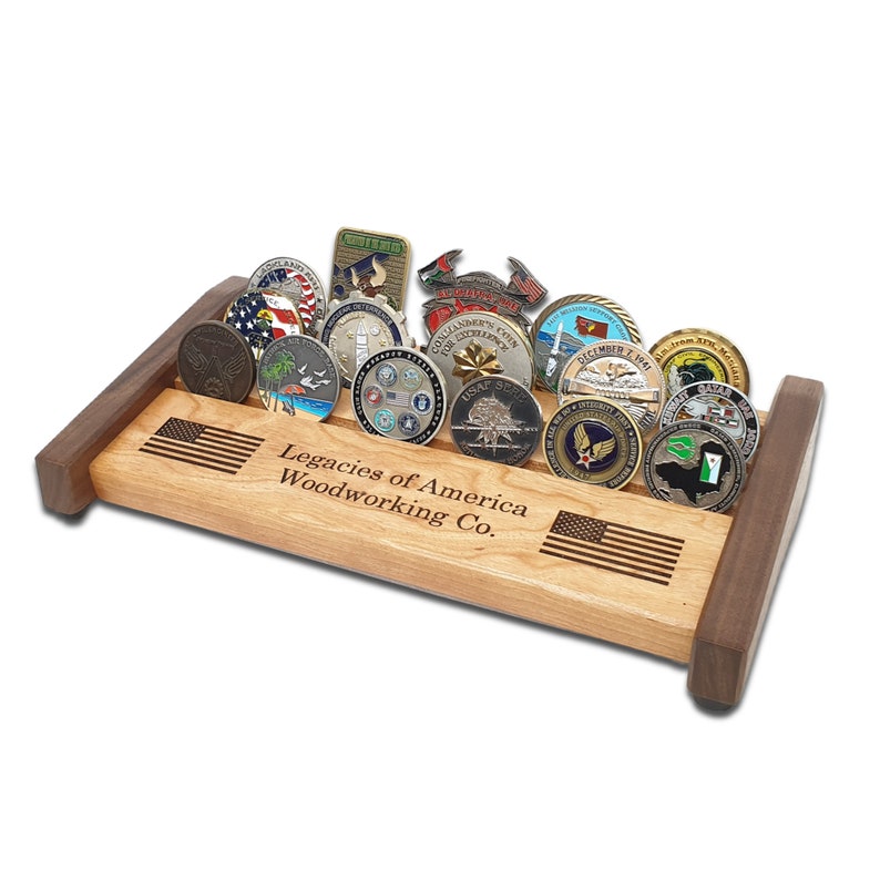 May include: A wooden coin display stand with an American flag design and the text "Legacies of America Woodworking Co.". The stand is filled with various military challenge coins.
