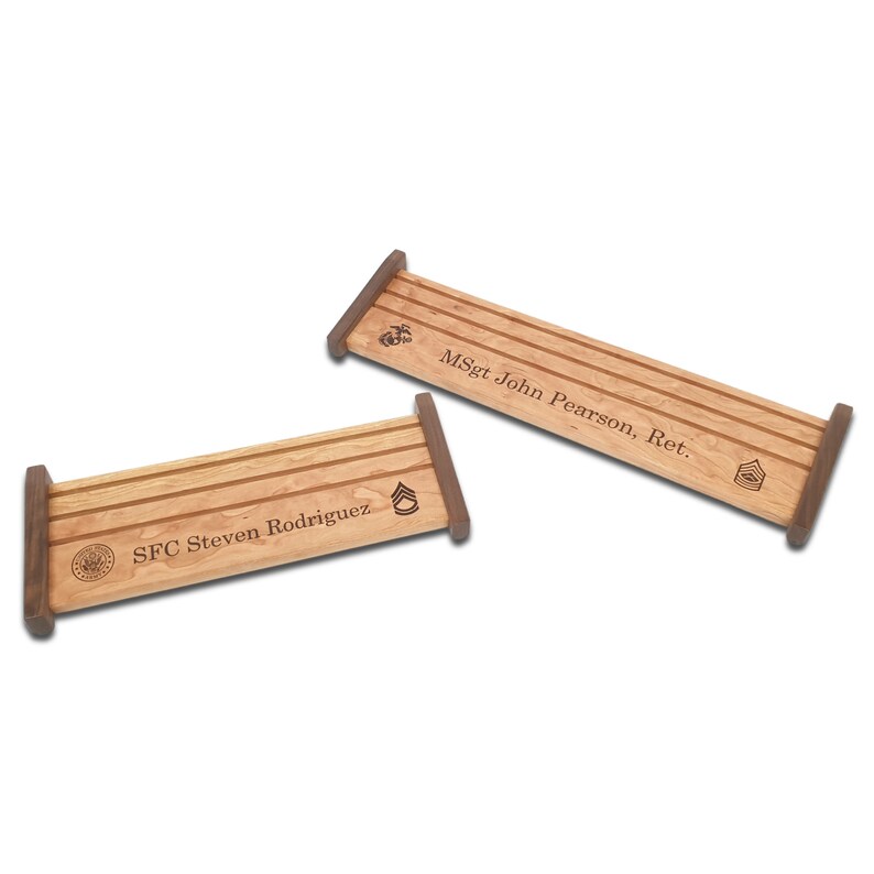 May include: Two wooden display stands with engraved names and military insignia. The top stand reads "MSgt John Pearson, Ret." and the bottom stand reads "SFC Steven Rodriguez".
