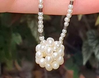 May include: A white pearl necklace with a small cluster of pearls at the end. The necklace is on a hand.