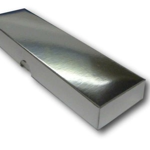 K&ouml;nnte beinhalten: Eine rechteckige silberne Schachtel mit einer glatten, gl&auml;nzenden Oberfl&auml;che. Die Schachtel ist aus Pappe und hat ein wei&szlig;es Innenleben.