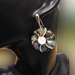 K&ouml;nnte beinhalten: Ein Paar silberne Ohrringe mit einem runden, schillernden Abalone-Muschel-Design. Die Muschel besteht aus mehreren Teilen von Abalone-Muschel, die einen Mosaik-Effekt erzeugen. Die Mitte der Muschel zeigt eine wei&szlig;e, spiralf&ouml;rmige Muschel.