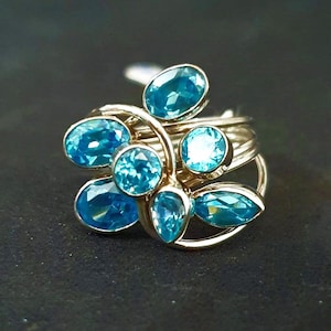 Könnte beinhalten: Ein silberner Ring mit einem Cluster aus blauen Edelsteinen, die in einem filigranen, wirbelnden Design gefasst sind.