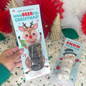 Op de afbeelding: Een kerstcadeau-label met een cartoon rendier en de tekst "Hope you have a WONDEERFUL CHRISTMAS!". Het label bevat een stapel donkergekleurde lekkernijen. Een tweede label toont een sneeuwpop.