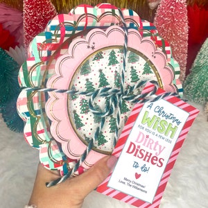 May include: A stack of decorative paper plates tied with twine, featuring a pink scalloped edge and a Christmas tree design. A gift tag reads "A Christmas Wish for you is a few less Dirty Dishes to do!"