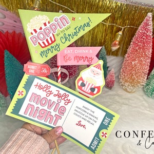 Puede incluir: Una colección de accesorios para fotomatón con temática navideña, que incluye letreros con textos como "Holly Jolly Movie Night" y "Eat, Drink & Be Merry". Los accesorios presentan colores y diseños festivos, con un gráfico de Papá Noel e imágenes de palomitas de maíz.
