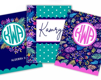 May include: Three notebooks with floral designs and personalized elements. One notebook has a teal monogram, another has the name "Kamry" in script, and the third has a pink monogram. The notebooks feature a variety of colors, including blue, teal, pink, and yellow.