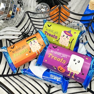 May include: A black web-shaped basket filled with Halloween-themed treats. The treats are wrapped in colorful packaging with the text "No tricks, just Treats" and cartoon characters. A blue and white candy bar is also in the basket.