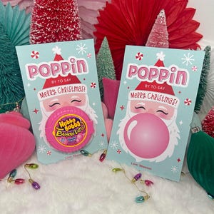 May include: Two Christmas cards with Santa Claus illustrations. The cards say "Poppin" and "Merry Christmas!" and feature a pink bubble gum. Festive decorations include ornaments and miniature Christmas trees.