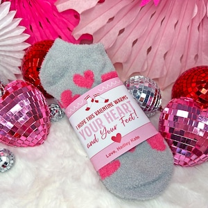 May include: A pair of gray fuzzy socks with pink hearts and a Valentine's Day gift tag that reads "I hope this Valentine warms your heart and your feet! Love, Hadley Kate."