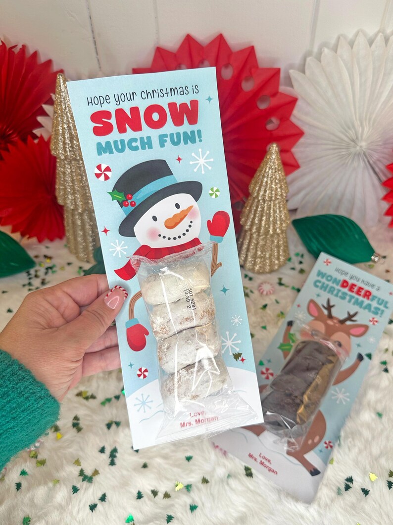 Op de afbeelding: Een lichtblauw kerstcadeaulabel met een sneeuwpopafbeelding en de tekst "Hope your christmas is SNOW MUCH FUN!". Het label bevat een doorzichtige zak met koekjes. Een tweede label toont een rendier.