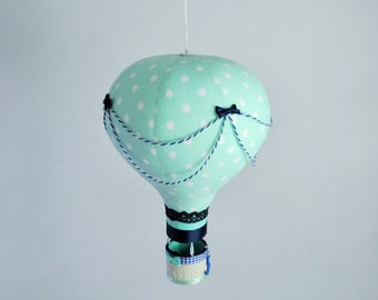 May include: A mint green hot air balloon with white polka dots and black ribbon accents hangs from a white cloud. The balloon has a blue and white striped basket.