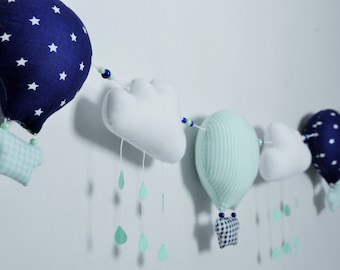 May include: A blue and white star patterned hot air balloon, a green and white striped hot air balloon, and two white clouds with blue beads hanging from a string.  Each balloon has a small, patterned fabric hanging from the bottom.
